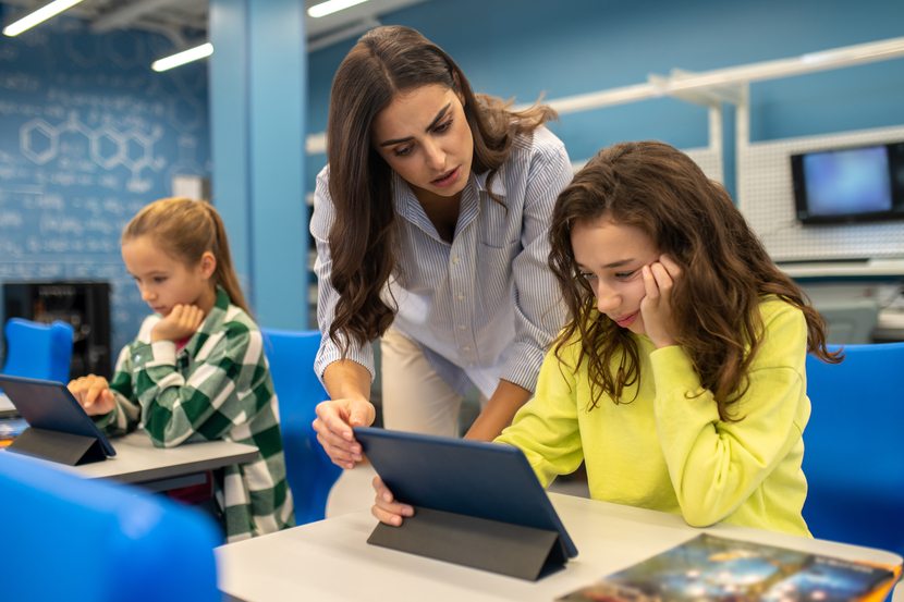 professora instruindo aluna em tablet na sala de aula