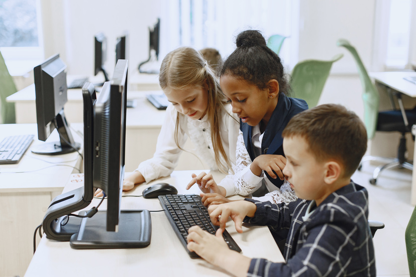 três crianças usando o computador na escola.