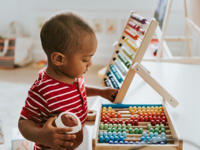 Criança brincando com ábaco colorido em ambiente de berçário.