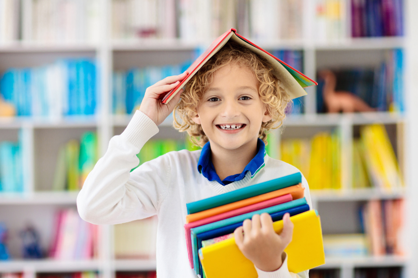 criança feliz com livro na mão e na cabeça