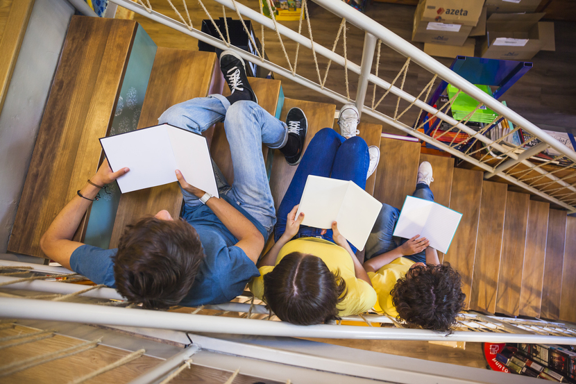 alunos de educação em tempo integral lendo livro na escada de uma biblioteca escolar 