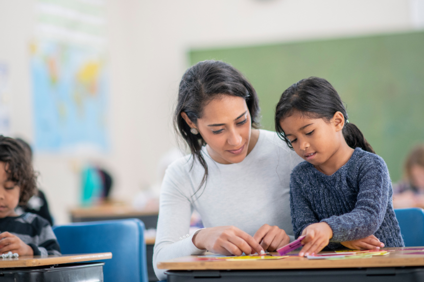 professora em carteira de aluna ajudando com atividade na sala de aula