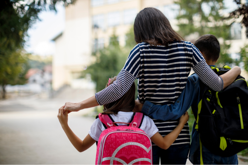 mãe abraçada com filhos indo pra escola